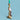 Gold candle holder with a parrot design holding a pink and green candle against a light blue background